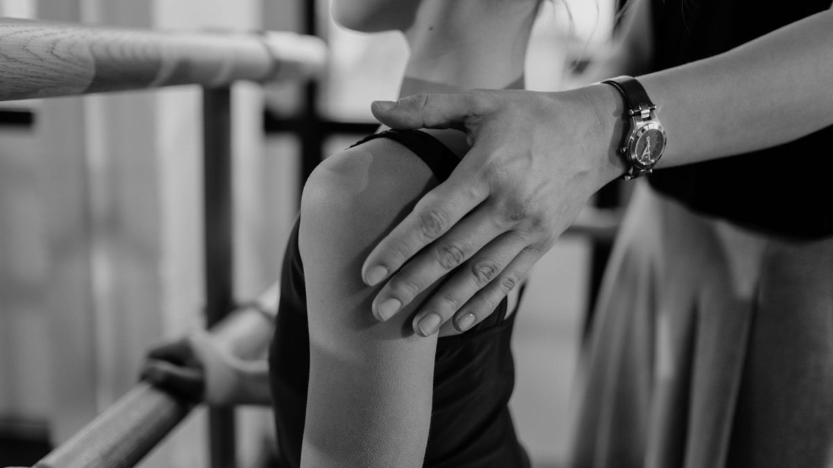 Main d'adulte corrigeant la posture de l'épaule d'une jeune danseuse
